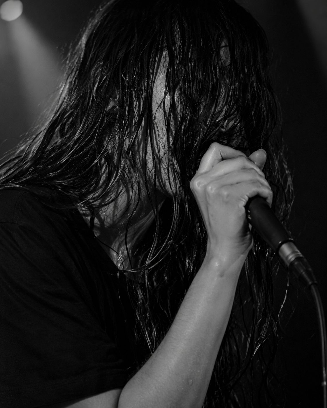 Close-up of a singer gripping a microphone, wet hair covering her face