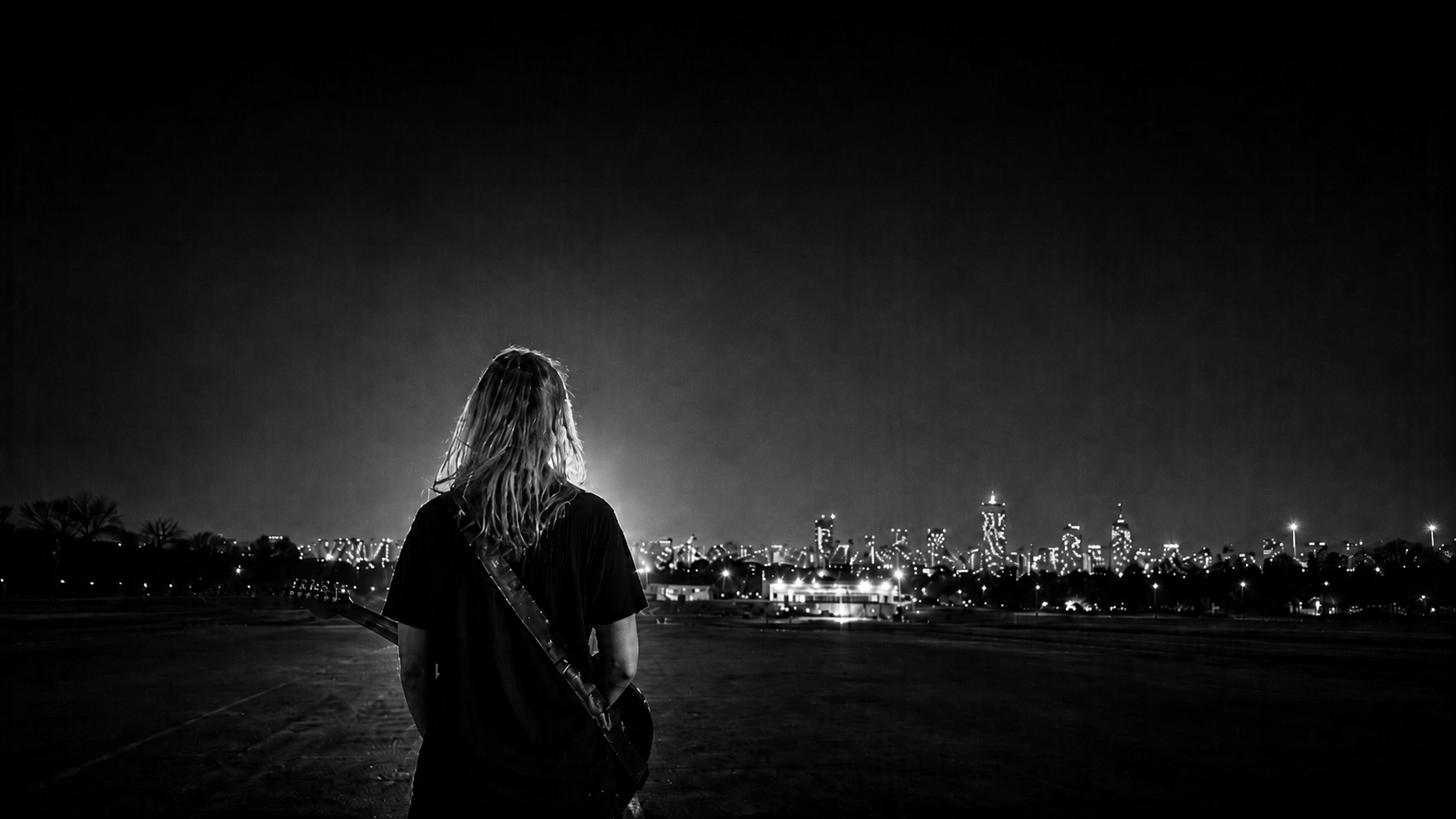 Jenny, seen from behind with a guitar on her back, facing a city skyline at night