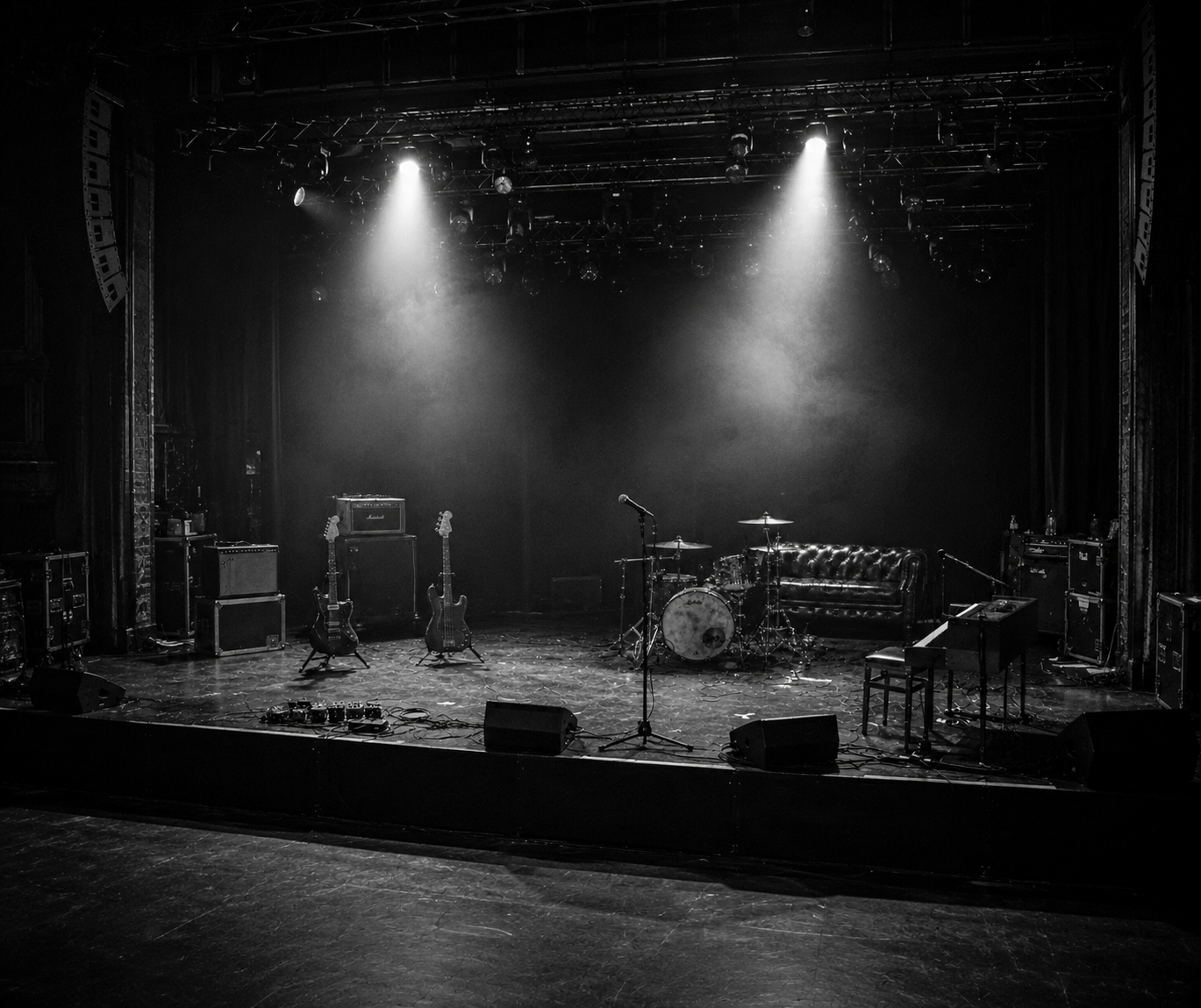 An empty stage under two spotlights: guitars, drums, piano and amps waiting